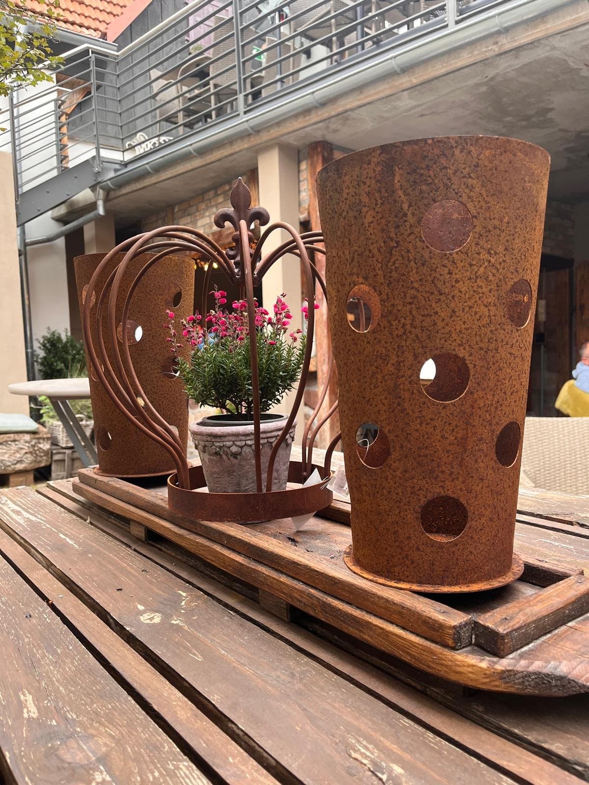 Dekoration aus Rost im Innenhof des Hofgarten Rosa: zwei Windlichter und eine Krone mit blühender Pflanze