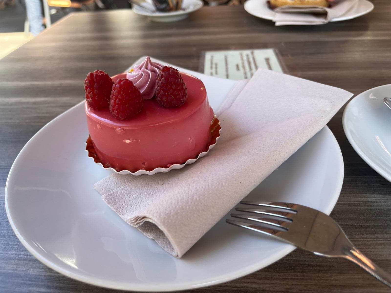 Himbeertörtchen mit rosa Glasur und frischen Himbeeren auf weißem Teller